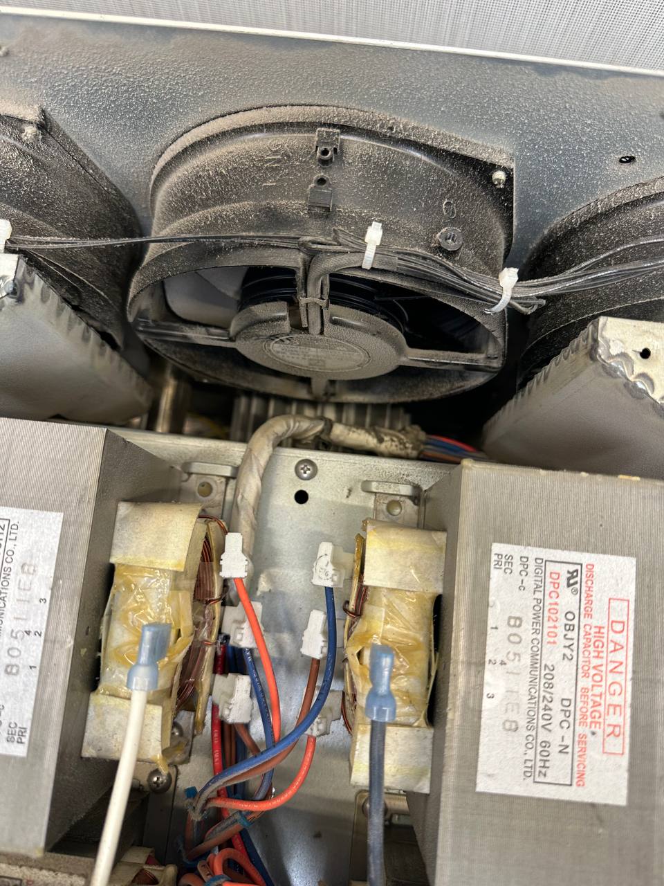 Dust-covered blower and fan housing with high-voltage components inside an oven, photographed during a service visit